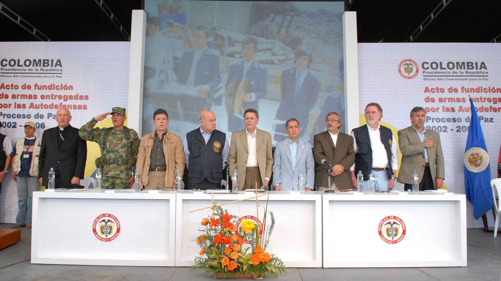 A row of men stand on stage behind a long table