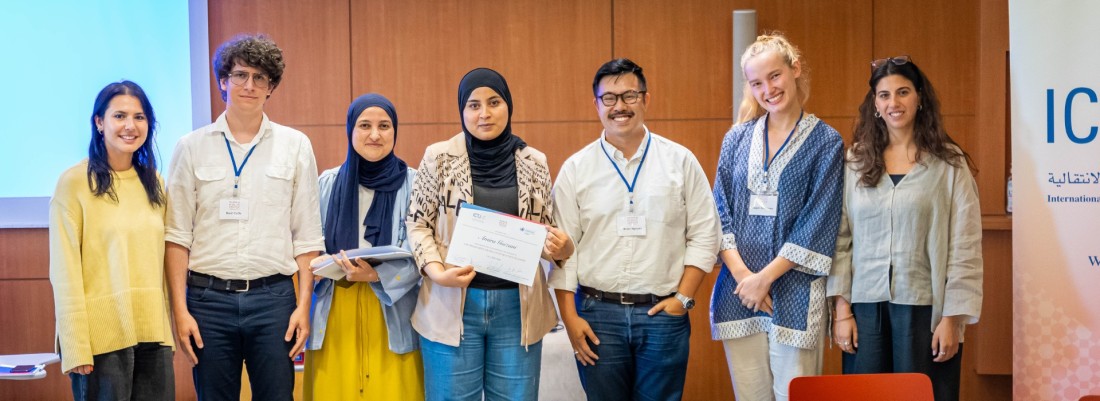 A standing woman holds a certificate flanked by several others. All smile facing the camera.