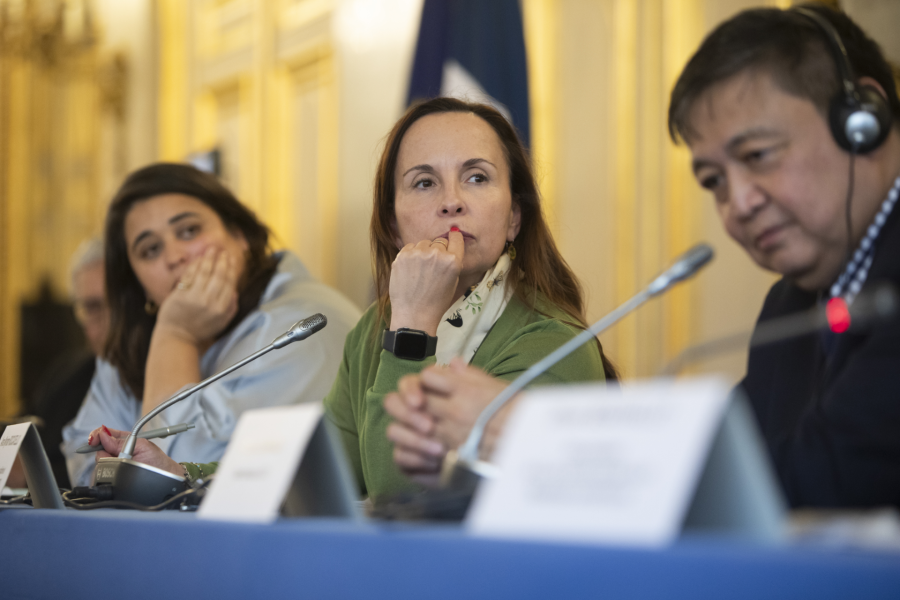 Three people sit a conference table, facing out toward the camera.