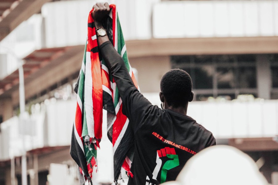 A man back facing camera holds up a Kenya flag