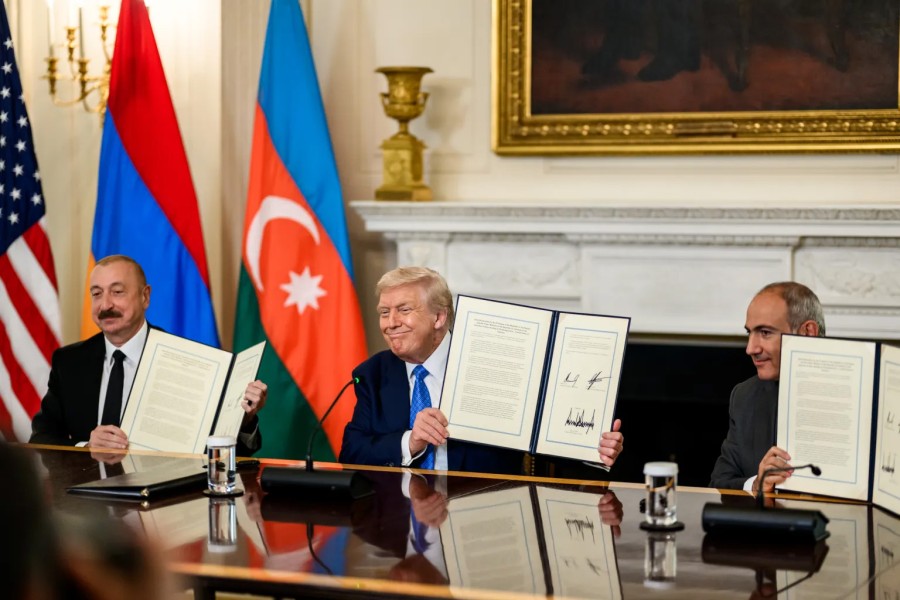 Armenian Prime Minister, Azerbaijani President, and U.S. President, seated at a table and wearing suits, each hold up a signed document in their hands