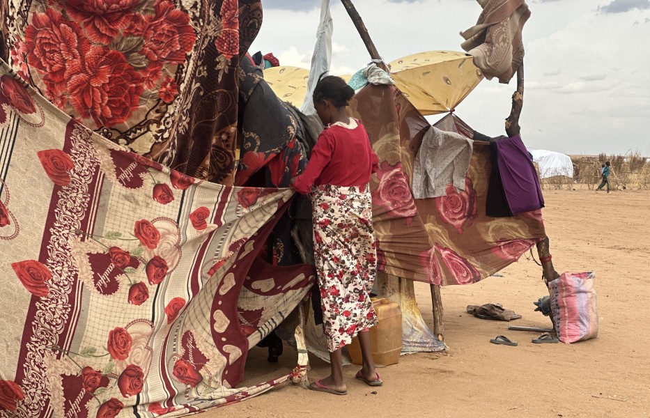 A woman builds a makeshift shelter made from tree branches and clothing.