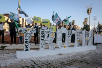 Demonstrators gather around a three-dimensional sculpture of the English word "Truth," waving placards. 