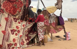 A woman builds a makeshift shelter made from tree branches and clothing.