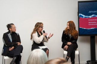 Three women sit on chairs facing a room holding microphones