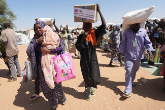 Men and women carry large boxes and sacks on their heads