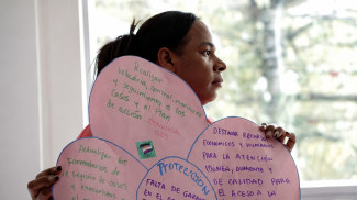 A person holds up a poater collage made up of pink paper with text in Spanish