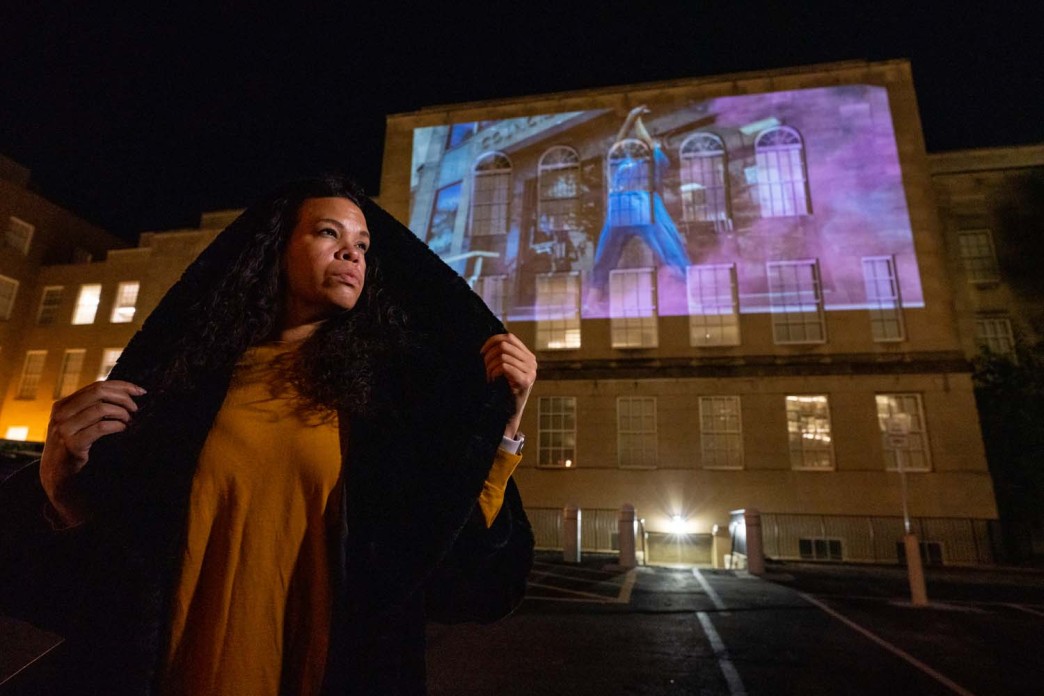 A woman stands in front of a courthouse on which a digital artistic display is being projected.