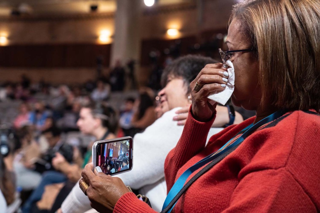 A woman in the audience wipes tears away with a tissue while she records the hearing with her cell phone.