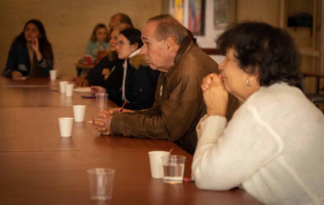 Several people sit on one side of a table, leaning intently forward as they listen.