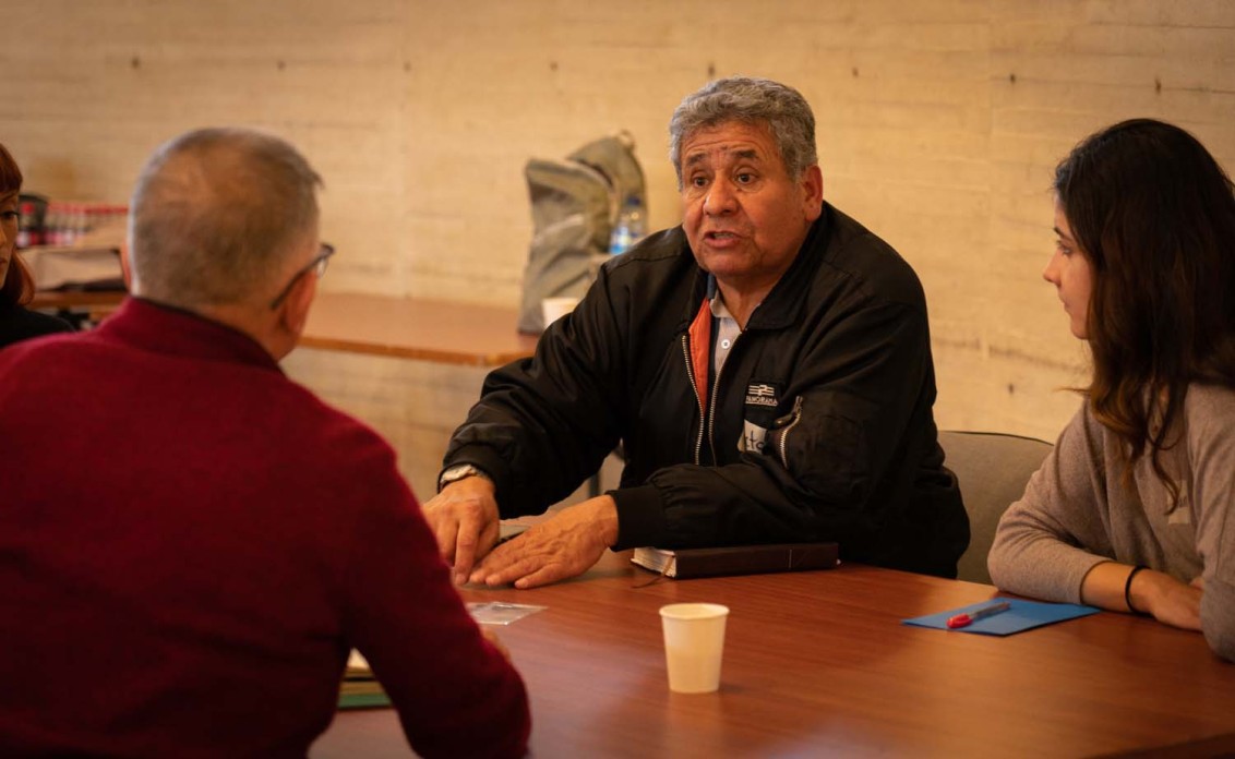 A man and a woman face another man across a table as they discuss something.