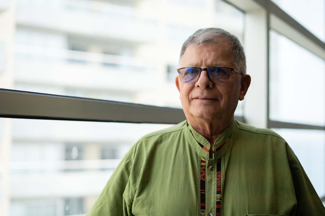 A man with tinted glasses and a green shirt looks just to the left of the camera.