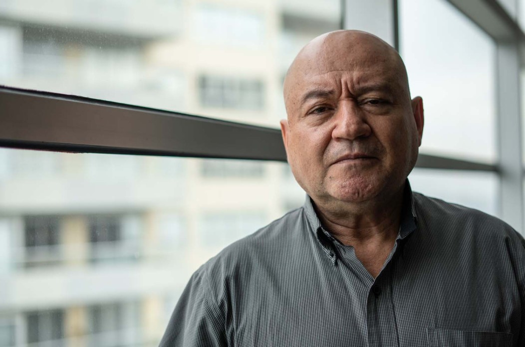 A bald man in a grey shirt gazes intently at the camera