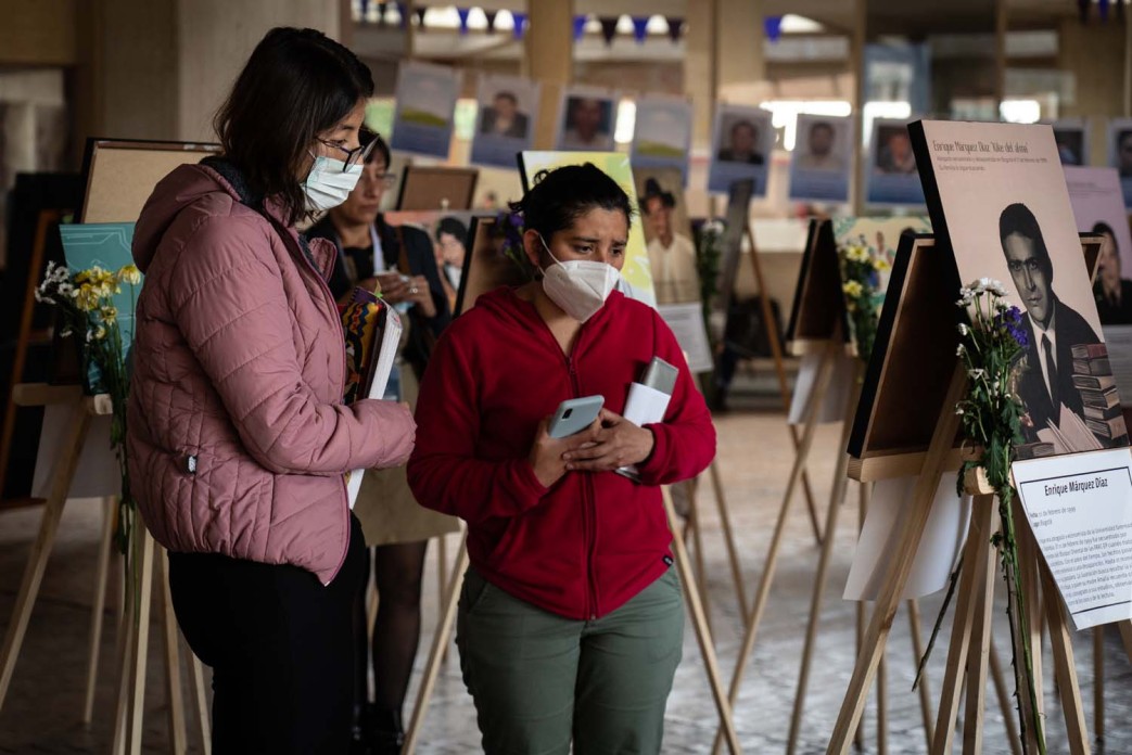 Three women stop to look at photos of people placed on easels.