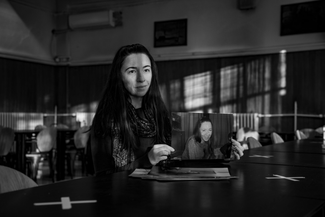 Une femme assise à une table tient une photographie 8x10 d'une femme qui lui ressemble.