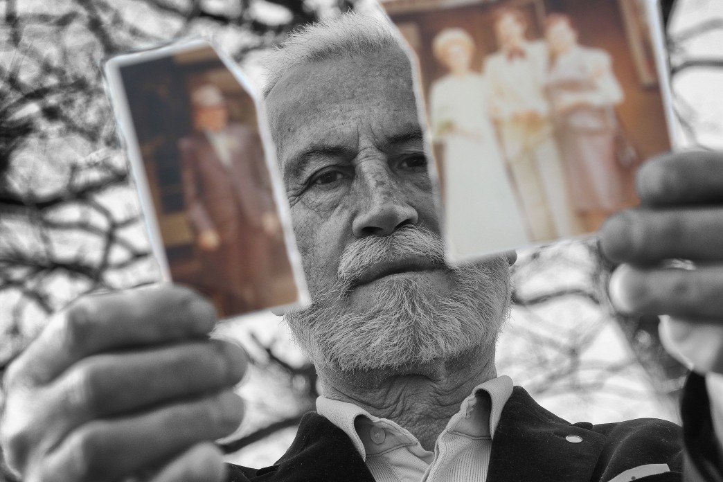 Un vieil homme tient deux moitiés déchirées d'une photographie et regarde entre elles.