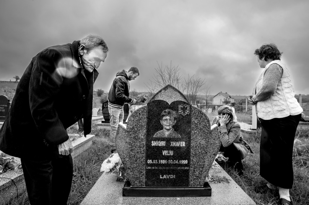 Une famille visite la pierre tombale d'un enfant, pleurant et déposant des fleurs.