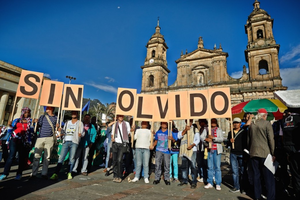 Protesters holding signs saying "SIN OLVIDO" in a square.